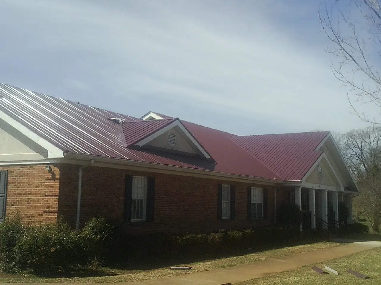 Red metal roof with gabled entries on a long brick building, from a Hail Damage Roof Repair job in Langley