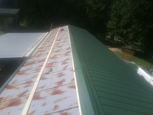 Old rusted panels beside newly installed green metal roofing — Wind Damage Roof Repair by Roofing Brothers in Langley