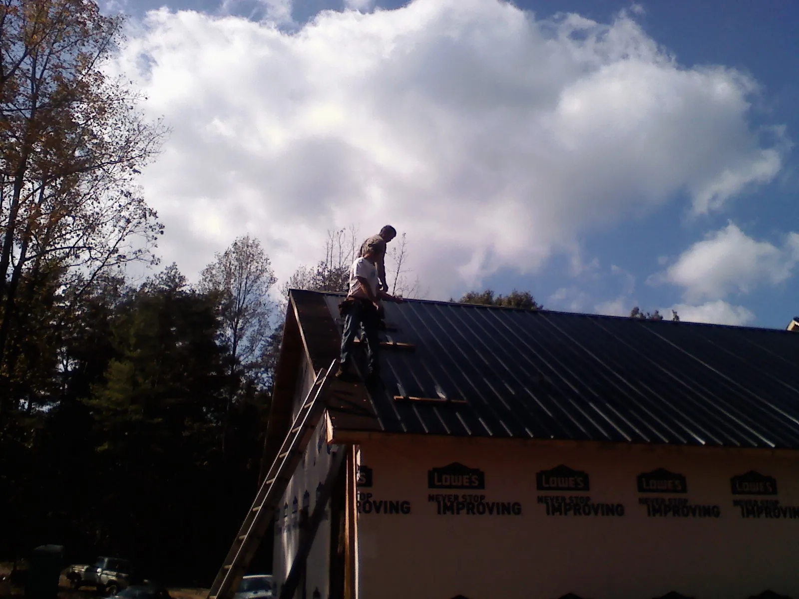 Roofer fastening dark metal panels high against a cloudy sky, from a Roof Inspection job in Langley